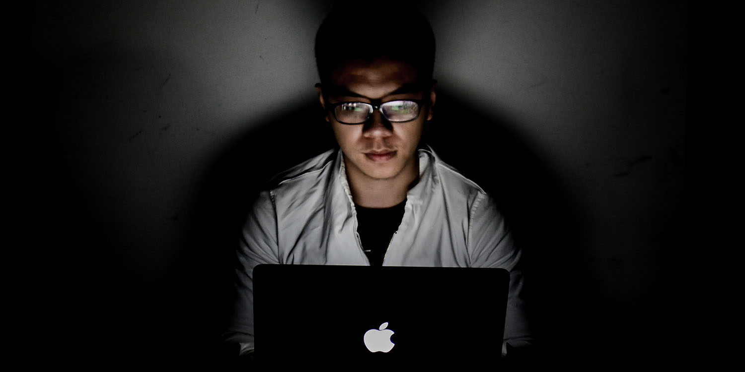 Spyware makers | Man in darkened room using MacBook