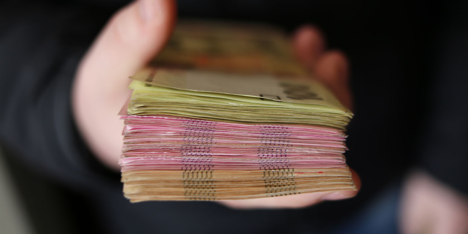 Scam loan apps | Hand holding out a large stack of currency
