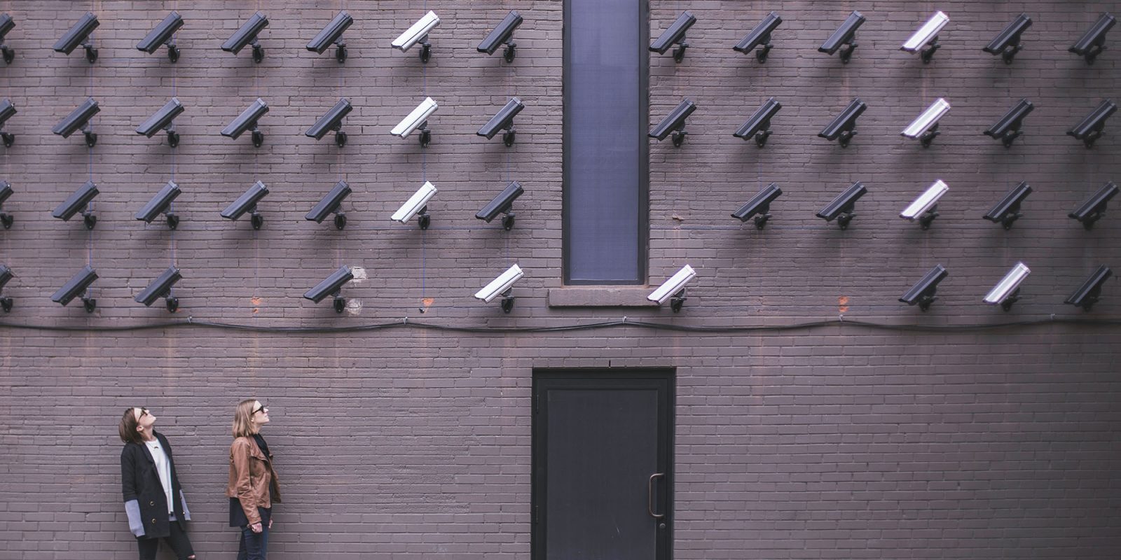 Reddit fighting back after AI fraud – but it could threaten user privacy | Two people looking up at a wall full of CCTV cameras