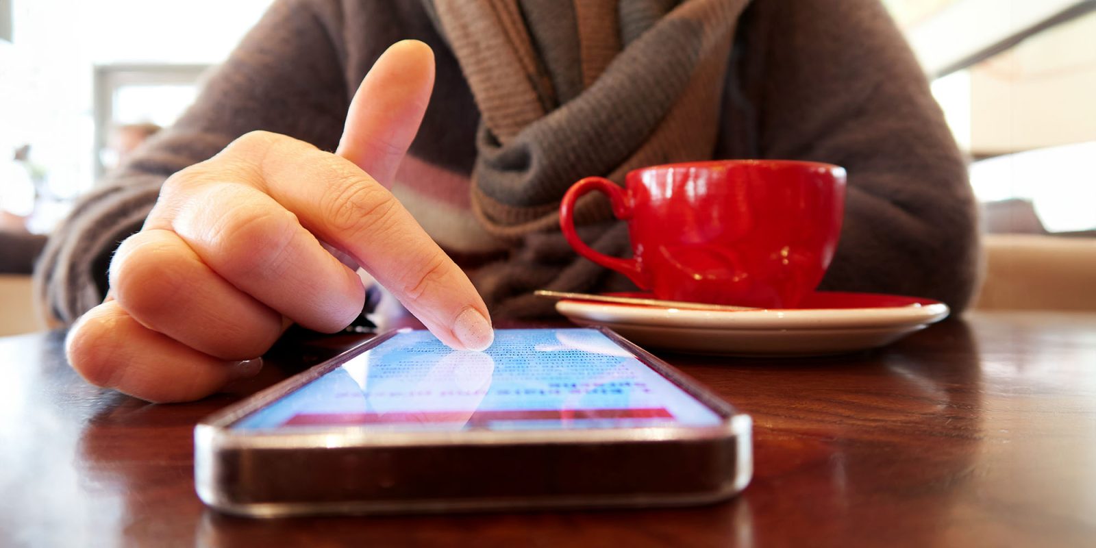 Right now is a good time to quit doomscrolling – here's how | Close-up photo of a finger scrolling on a smartphone screen while drinking coffee